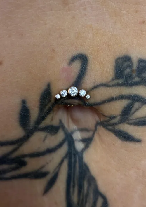 Tatuaj negru floral în jurul unui piercing cu pietre strălucitoare la buric